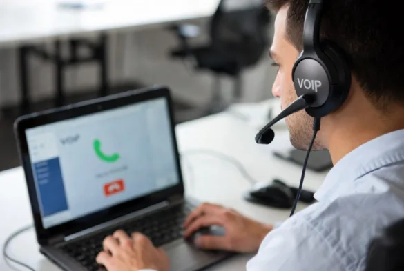 Office worker answering a VoIP call on a laptop with headset